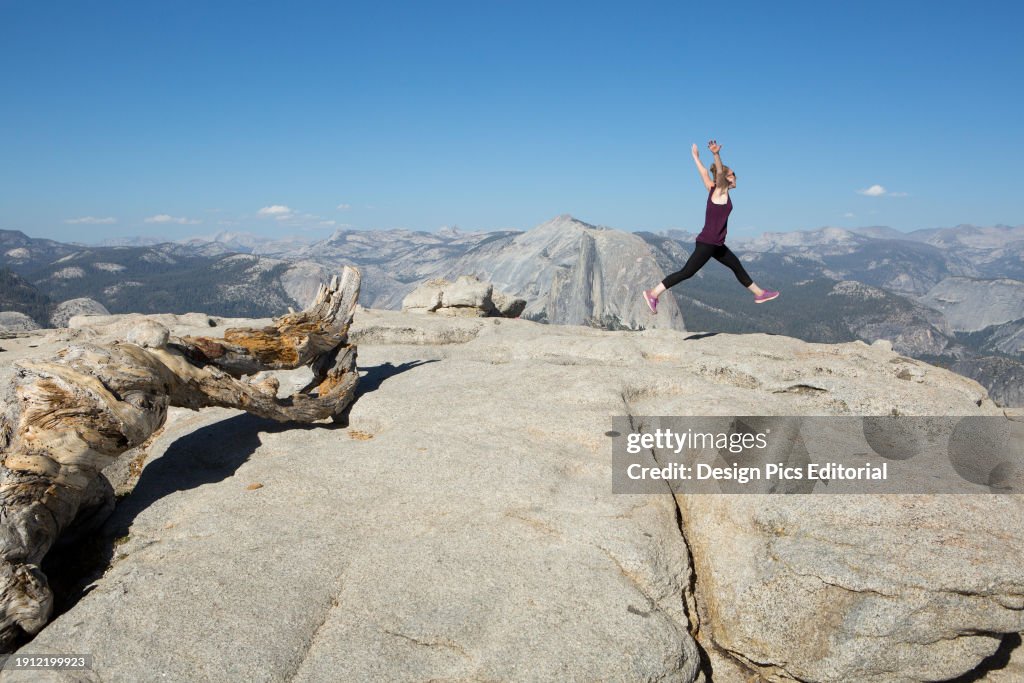 A hiker gracefully jumps, in a ballet motion, atop Sentinel Dome, a rocky peak that offers stunning views to the Yosemite Valley.; Yosemite National Park, California