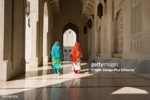 Two traditionally dressed women walking through a corridor of the Sultan Qaboos Grand Mosque. Muscat, Oman.