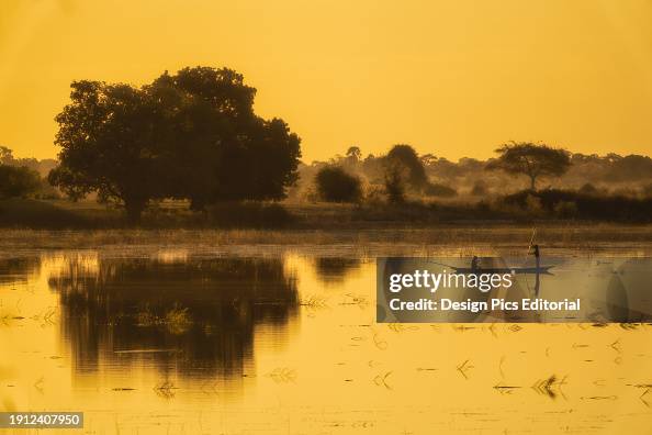 Fishermen collecting their nets at sunset off the Chobe River with the golden sky reflected in the tranquil water; Botswana