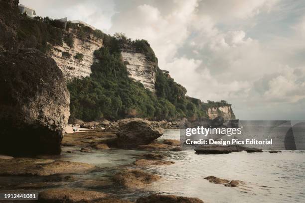 Rugged cliffs and foliage along a coastline with cloud formations in the sky, Diamond Beach. Nusa Penida, Bali, Indonesia.