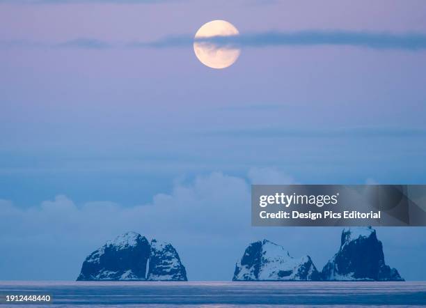 Full moon sets over two mountainous islands in the Gerlache Strait off the coast of the Antarctic peninsula. Antarctica.