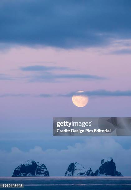 Full moon sets over two mountainous islands in the Gerlache Strait off the coast of the Antarctic peninsula. Antarctica.