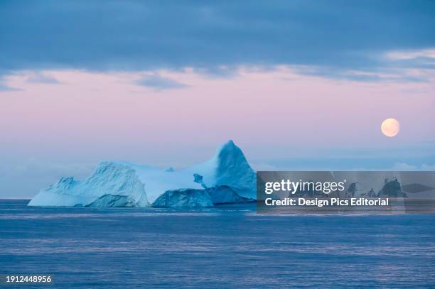 Full moon sets over icebergs and mountainous islands in the Gerlache Strait off the coast of the Antarctic peninsula. Antarctica.