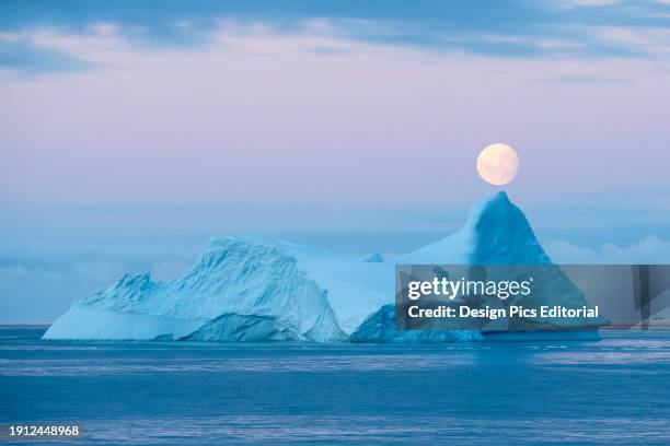 Full moon sets over an iceberg in the Gerlache Strait off the coast of the Antarctic peninsula. Antarctica.