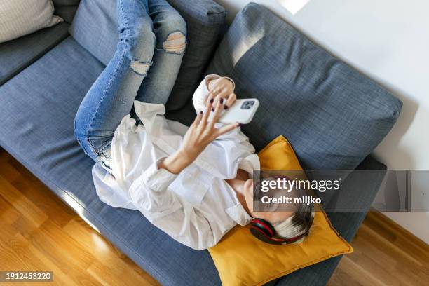 una giovane donna sdraiata sul divano che ascolta musica con le cuffie - supino foto e immagini stock