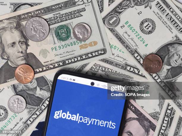 In this photo illustration, a Global Payments logo seen displayed on a smartphone with United States Dollar notes and coins in the background.