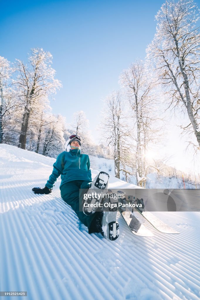 A female skier enjoys a scenic view while sitting on snow in a mountain forest in sunny weather