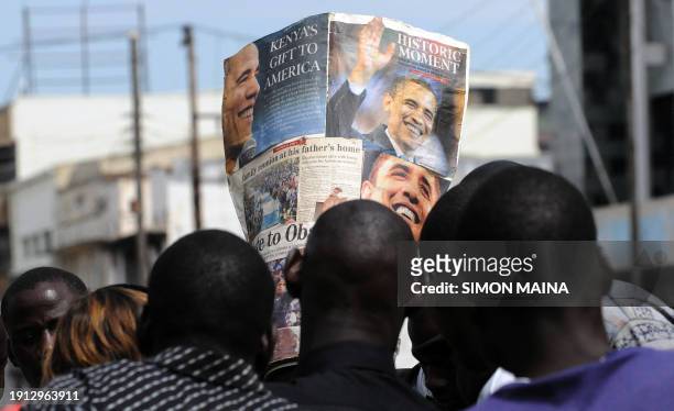 Kisumu residents look on November 3, 2008 at a man wearing a hat made from newspapers clippings of US Democratic presidential candidate Barack Obama...