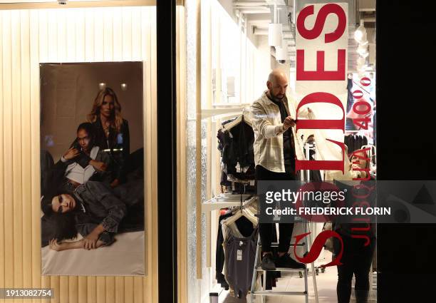 Workers hang an advertising banner announcing the Winter Sales on the eve of their official start in Strasbourg, eastern France, on January 9, 2024.