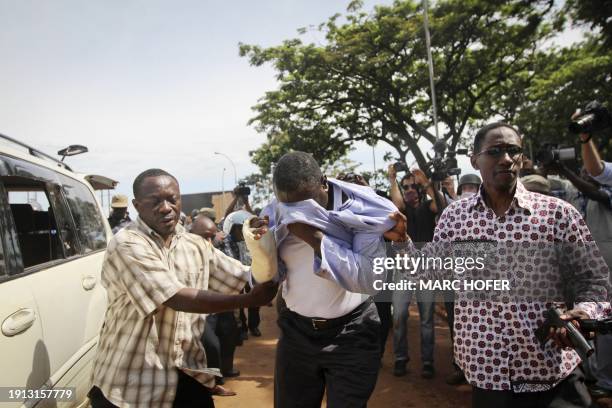Opposition leader Kizza Besigye wipes his face while he is dragged away by two Ugandan plainclothes policemen while being arrested for the fourth...