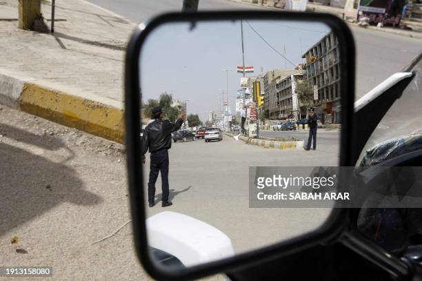 Iraqi traffic policemen are reflected in a mirror as they stand in a street in central Baghdad on March 6, 2010 a day before the country's general...