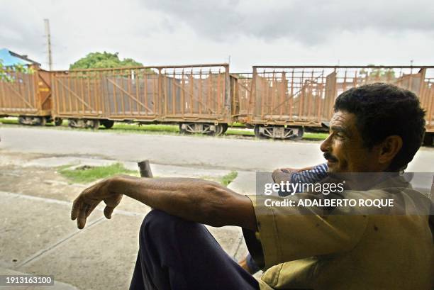 Man sits in front of wagons that used to trasnport sugar, in San Luis province of Santiago, Cuba, 09 June 2002. AFP PHOTO/Adalberto ROQUEUn hombre...