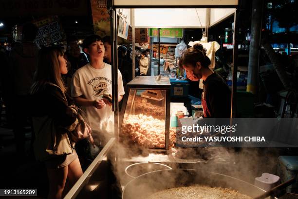 This photo taken on January 9, 2024 shows a woman preparing fried chicken for customers at the Shanhua night market in Tainan.