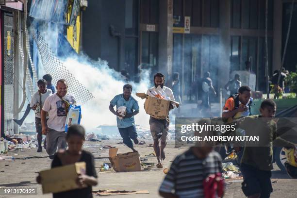 People run with merchandise as crowds leave shops with looted goods amid a state of unrest in Port Moresby on January 10, 2024. A festering pay...