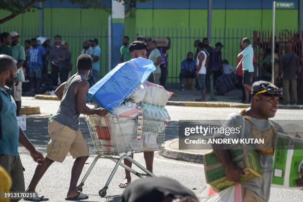 Man pushes a shopping trolley on the street as crowds leave shops with looted goods amid a state of unrest in Port Moresby on January 10, 2024. A...