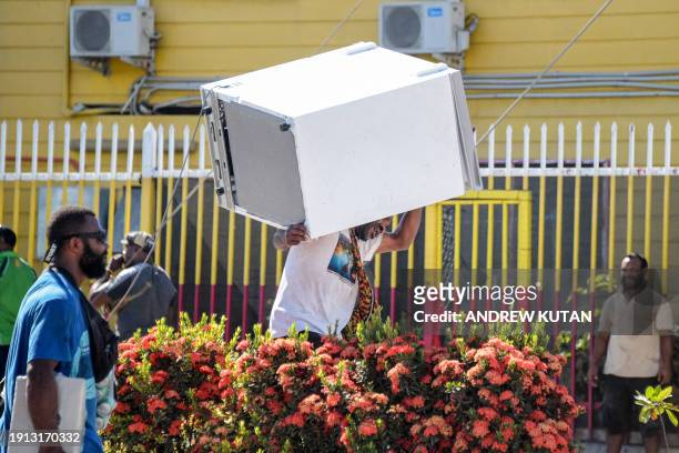 Man carries a freezer as crowds leave shops with looted goods amid a state of unrest in Port Moresby on January 10, 2024. A festering pay dispute...