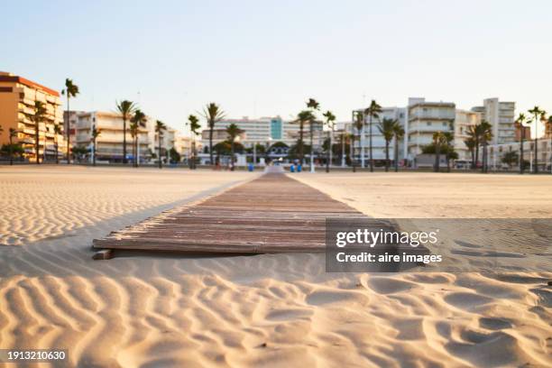front view of a wooden path in the middle of the beach without people with buildings in the background - boardwalk stock pictures, royalty-free photos & images