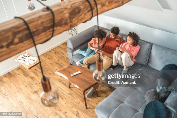 diverse father and daughters reading a book in a living room - family and happiness and diverse imagens e fotografias de stock