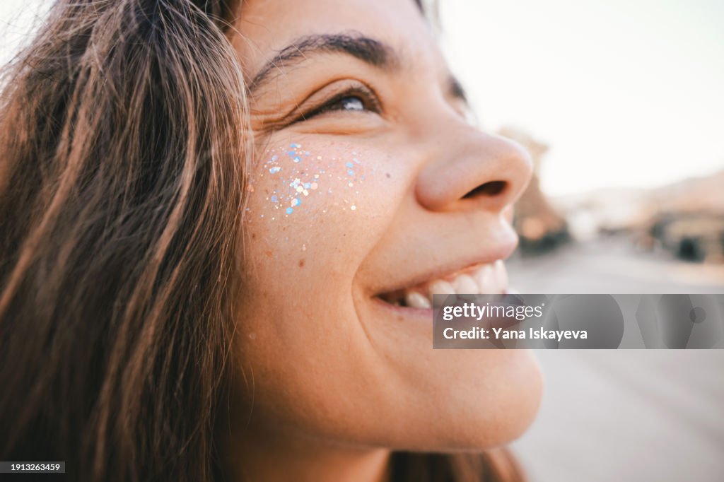 A funny wide angle portrait of a cute young woman with glitter sprinkled on her cheeks. Positive emotions, optimistic attitude, and humor