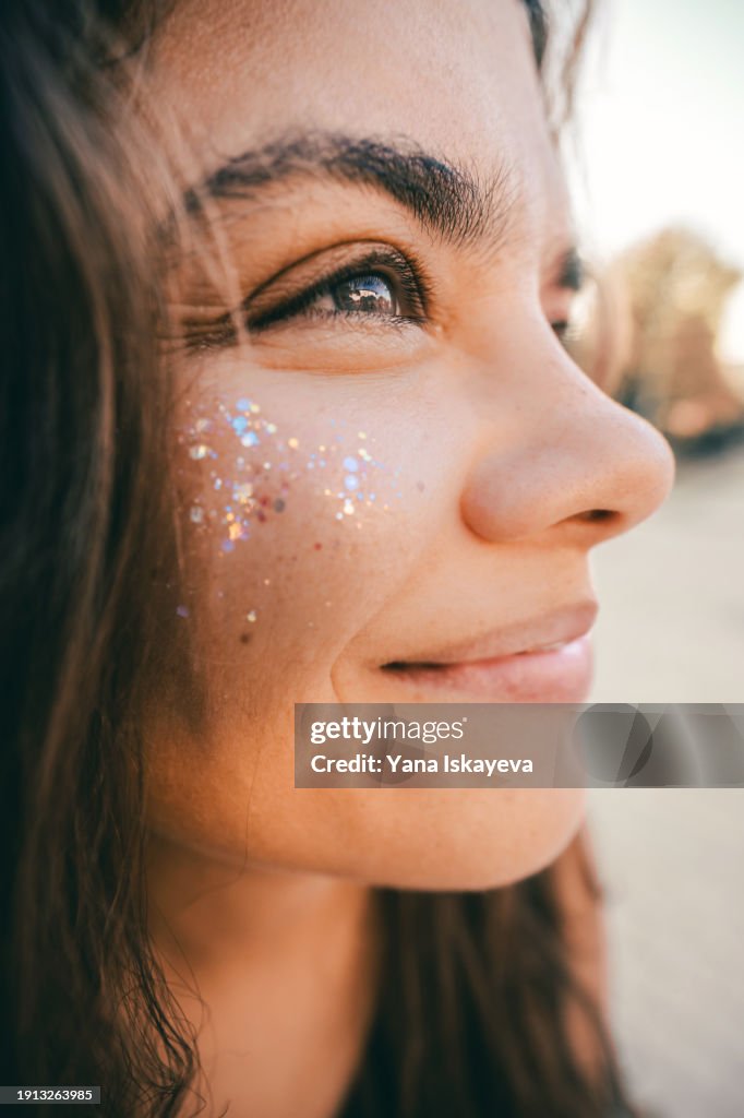A funny wide angle portrait of a cute young woman with glitter sprinkled on her cheeks. Positive emotions, optimistic attitude, and humor