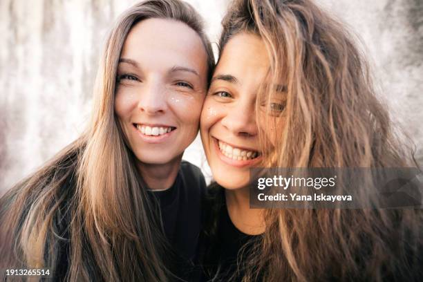 a funny wide angle selfie of two diverse friends looking at camera, laughing. a fancy multicolor glitter on their young skin - oxytocin stock pictures, royalty-free photos & images