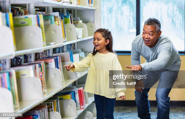 asian father, multiracial girl look for book in library - mirar alrededor fotografías e imágenes de stock