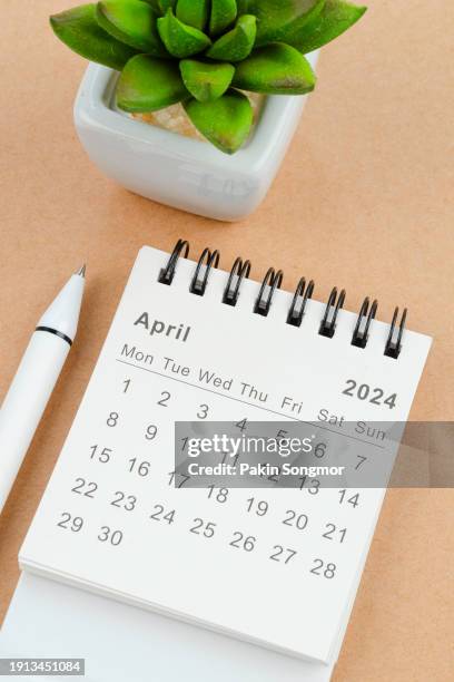 desk calendar 2024: april calendar is used to plan daily work and life with houseplant and white pen against a brown background. - april stock pictures, royalty-free photos & images