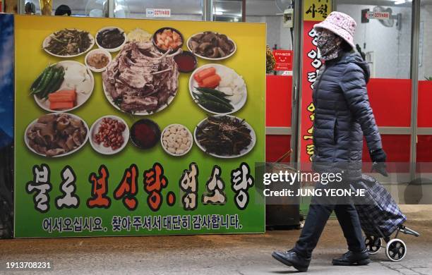 Woman walks in front of an advertising poster showing dog meat dishes in Daegu on January 10, 2024. South Korea's parliament on January 9, passed a...