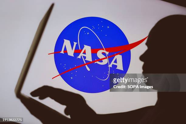 In this photo illustration, the National Aeronautics and Space Administration logo is seen in the background of a silhouette of a person using a...
