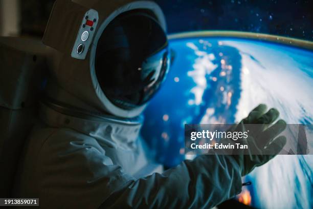 asian chinese mid adult female astronaut looking at earth through window from spaceship at outer space - astronaut bildbanksfoton och bilder