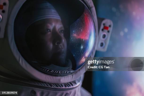 asian chinese mid adult female astronaut looking at earth through window from spaceship at outer space - cosmonauta fotografías e imágenes de stock