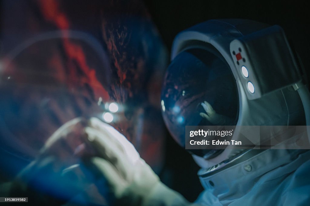 Asian chinese mid adult female astronaut looking at earth through window from spaceship at outer space