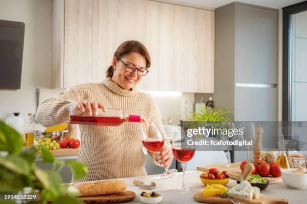 portrait of a happy woman pouring rose wine into a glass - day in the life series stock pictures, royalty-free photos & images
