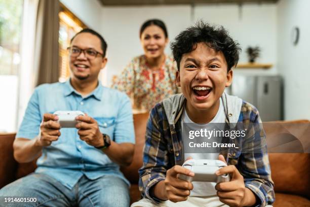 south east asian family at home, playing video games with game controllers. teenage boy winning against father - indonesian ethnicity stock pictures, royalty-free photos & images