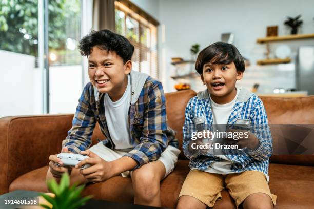 south east asian brothers playing video games at home - videospel stockfoto's en -beelden