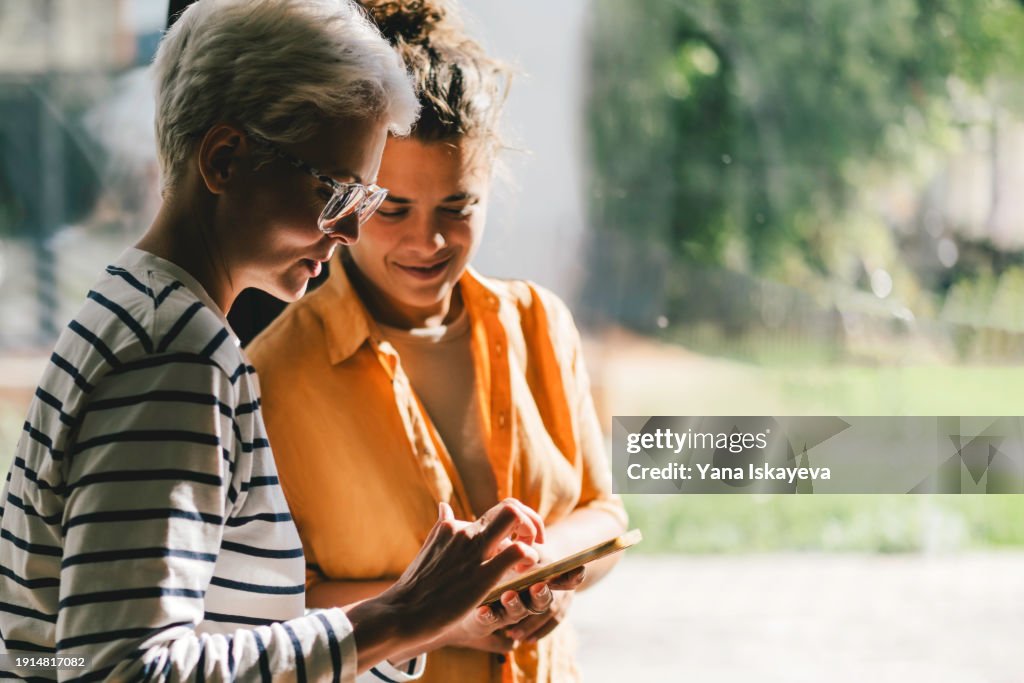 A shared moment in techology. Two middle aged women in a neutral surroundings interacting with a smartphone and talking each other