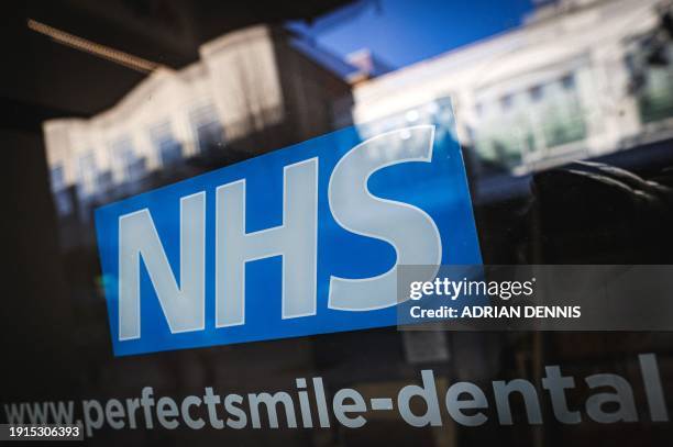 Photograph taken on January 10, 2024 shows the logo of the NHS on the window display of a dental surgery, in Bracknell.