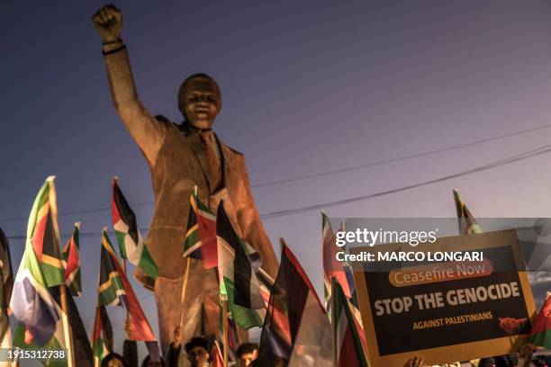 People raise flags and placards as they gather around a statue of late South African president Nelson Mandela to celebrate a landmark "genocide" case...