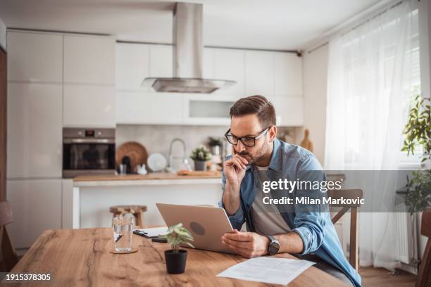 a young man works from home using a laptop - portrait of pensive young businessman wearing glasses stock-fotos und bilder