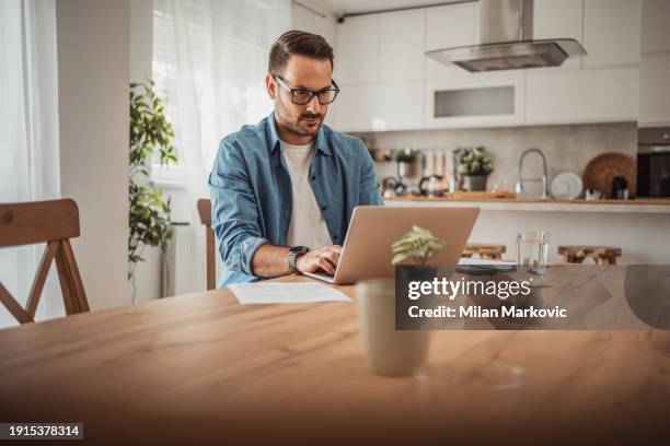 a young man works from home using a laptop - portrait of pensive young businessman wearing glasses stock pictures, royalty-free photos & images