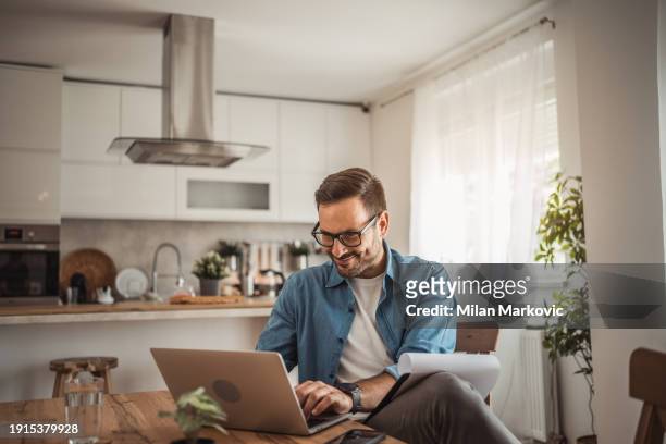 a young man works from home using a laptop - portrait of pensive young businessman wearing glasses stock-fotos und bilder