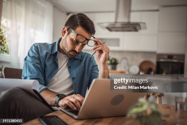 a young man works from home using a laptop - portrait of pensive young businessman wearing glasses stock-fotos und bilder