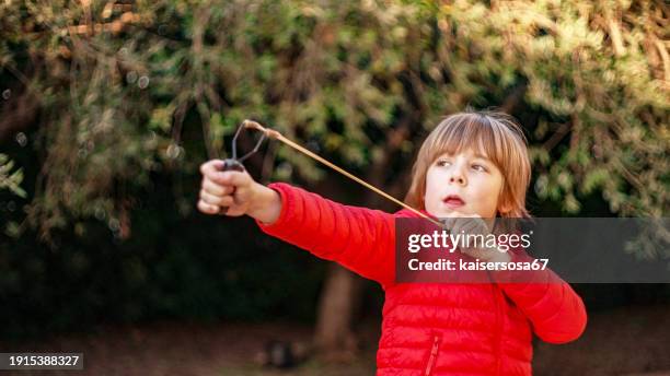 7 year old boy enjoys playing with the slingshot outdoors - slingshot stock pictures, royalty-free photos & images