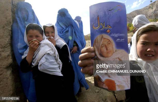 An Afghan schoolgirl displays a leaflet distributed by presidential candidate Masooda Jalal while woman villagers and fellow schoolgirls shy away...