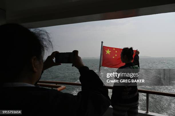 Chinese tourist poses for photos with the Chinese flag, with the backdrop of Taiwanese islands from a distance of 2 kilometers, during a boat tour to...