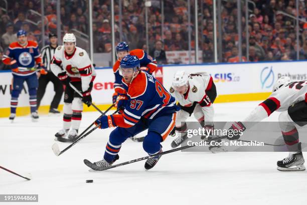 Connor McDavid of the Edmonton Oilers skates past Tim Stutzle and Travis Hamonic of the Ottawa Senators during the first period at Rogers Place on...