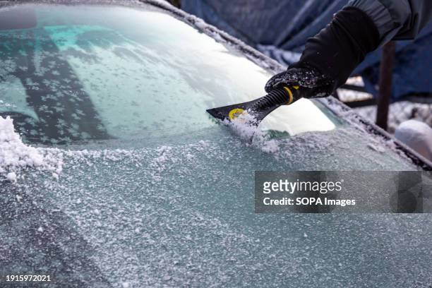 Man clears snow and ice from his car as the temperature drops below zero.