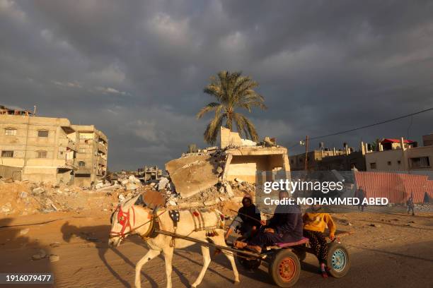 Palestinian man rides a donkey-pulled cart on January 11, 2024 near a destroyed building which was hit in an Israeli air strike, in Rafah in the...