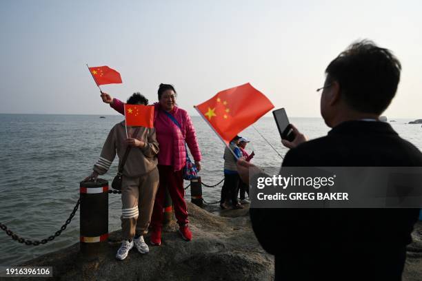 Chinese visitors take photos with Chinese flags, with Taiwan's Kinmen Island as a background, on the beach at Xiamen, in China's southeast Fujian...