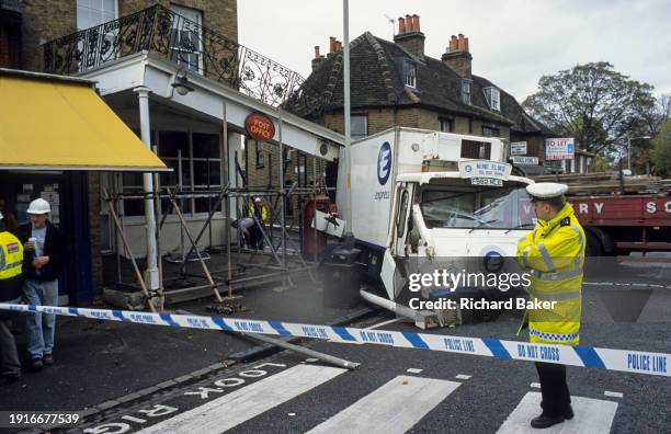 With a police officer looking on, a milk delivery vehicle has crashed into the corner of the roof awning of the local Post Office in Dulwich Village,...